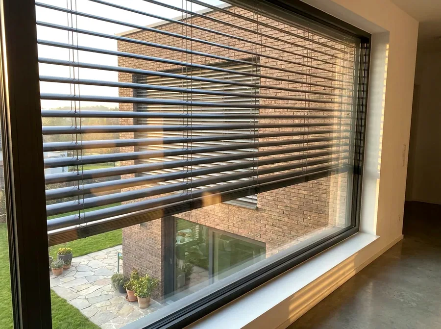 External aluminium venetian blinds mounted outside the glass on a Bedfordview facade, slats angled against low afternoon sun with a neighbouring face-brick home beyond